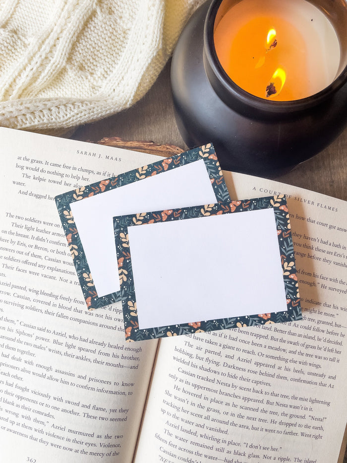 These floral faerie garden post-it notepads have a teal background with yellow and light sage green foliage and little orange celestial butterflies on them. Design is only around the border.